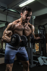 Naklejka na ściany i meble White Muscular man training his biceps in the gym by dumbbells
