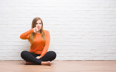 Young adult woman sitting on the floor in autumn over white brick wall with angry face, negative...