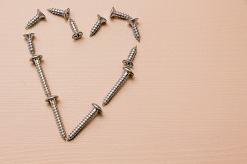 Self-tapping screw shaped like a heart on a wooden background