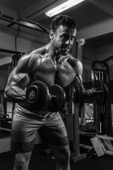 Plakat White Muscular man training his biceps in the gym by dumbbells BW