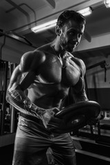 Fototapeta na wymiar White Muscular man is posing in gym with weight plate and straining muscles BW