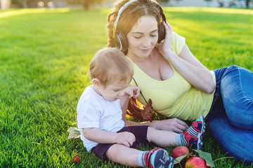 Beautiful modern mom playing in a green meadow with her cute baby son in a Sunny Park. Concept of the joy of motherhood