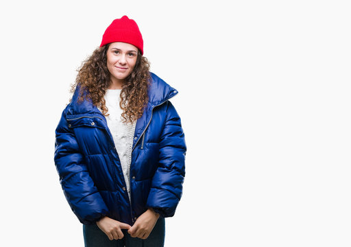 Beautiful young brunette curly hair girl wearing winter coat, wool cap and sweater over isolated background with a happy and cool smile on face. Lucky person.