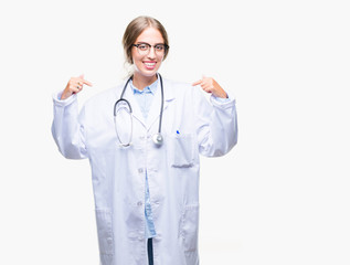 Beautiful young blonde doctor woman wearing medical uniform over isolated background looking confident with smile on face, pointing oneself with fingers proud and happy.