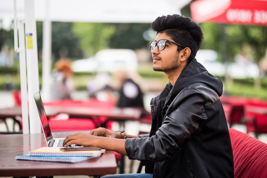 Young Indian Man Working On Laptop While Sitting In Street Cafe