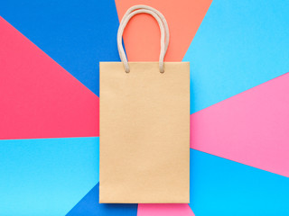craft paper shopping bag on colorful geometric background. store sale and consumerism. empty space...