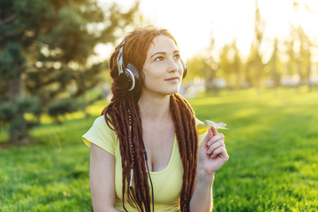 Modern girl with dreadlocks listening to music with her headphones in autumn Sunny Park. Favorite music, happy time.