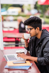 Indian Man using laptop computer while drinking a cup coffee, outdoor street cafe