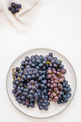 Berries of ripe blue grapes on a plate on a table. Harvesting in autumn. Top view