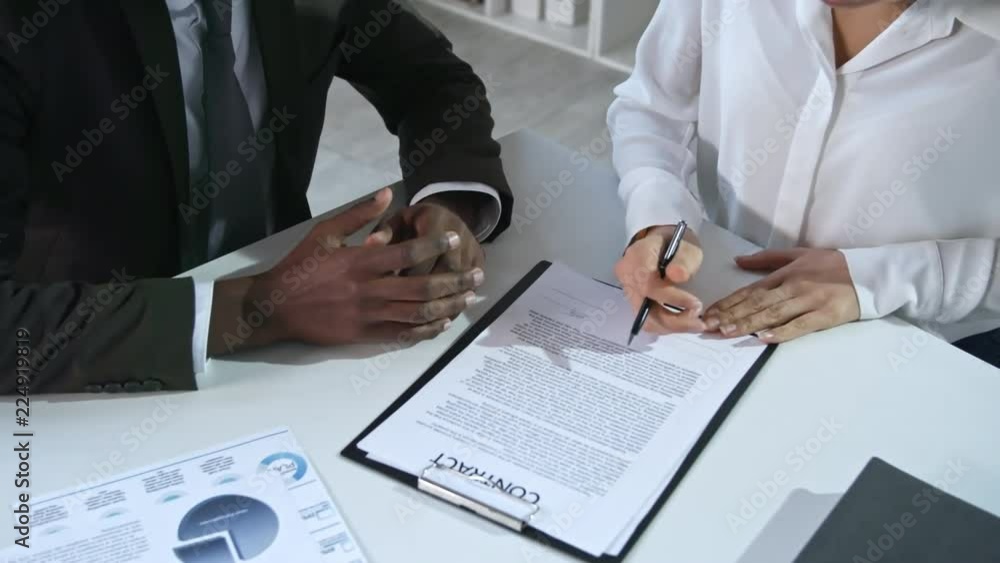 Poster High angle view of two multi ethnic office workers signing contract and shaking hands when sitting at desk in office during meeting