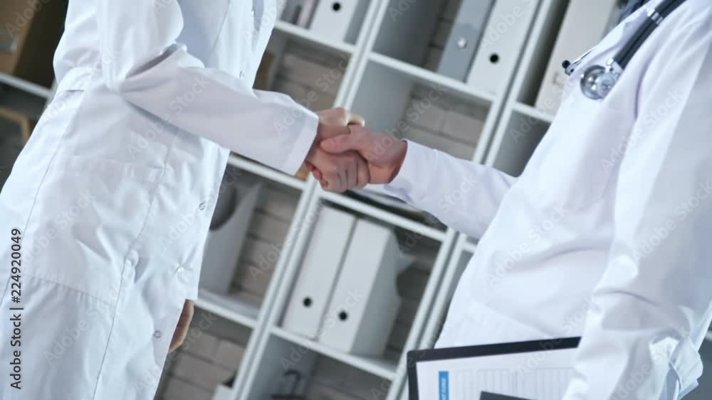 Poster dutch angle view of two unrecognizable specialists in lab coats approaching each other and shaking h
