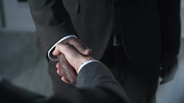 Extreme close up of two unrecognizable businessmen of different ethnicities shaking hands to seal the deal