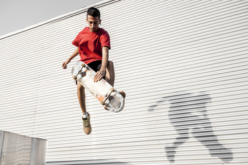 young skateboarder jumps up with his board in front of a metal background