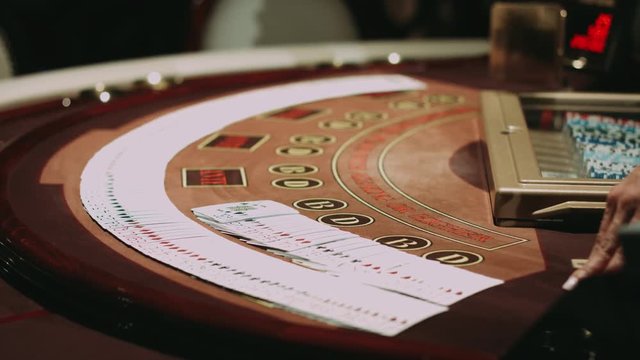 Blackjack dealer during cards shuffle on gambling table. Close up professional croupier hands showing playing cards. Poker table brown surface with classic betting grid. Gambling game in casino