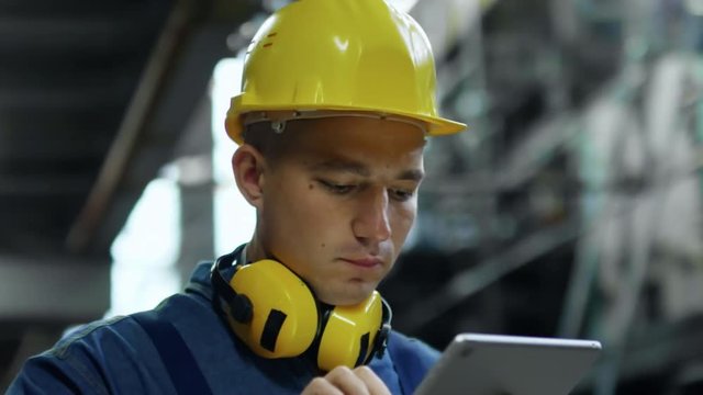 Close up face of hardworking man in bump cap using tablet computer application when working in industrial building