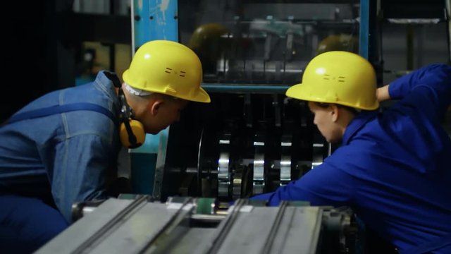 Medium shot of two factory workers in yellow protective helmets trying to repair printing machine