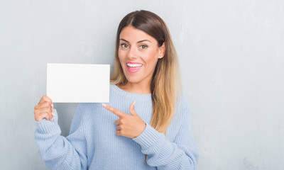 Naklejka premium Young adult woman over grey grunge wall holding blank card very happy pointing with hand and finger