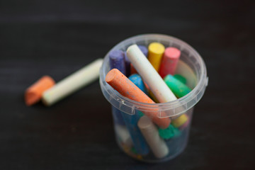 Color chalk in plastic cans closeup on blackboard. Selective focus