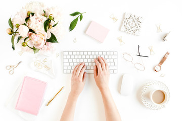 Flat lay women's office desk. Female workspace with female hands, computer, pink peonies bouquet, accessories on white background. Top view feminine background.