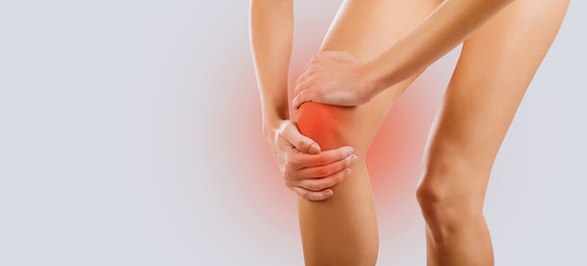 Pain, injury to the knee. A woman holds her knee with her hand.