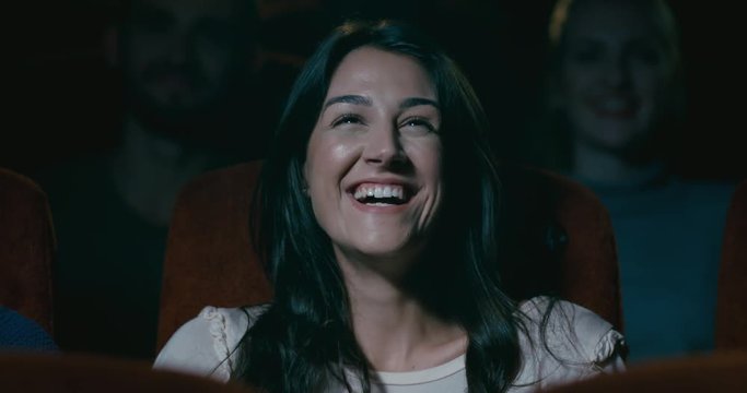 Woman in a movie theatre laughing uncontrollably as she watches a very funny film