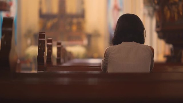 Back view of religious Christian woman sitting in the church while praying to GOD. Shot in 4k resolution