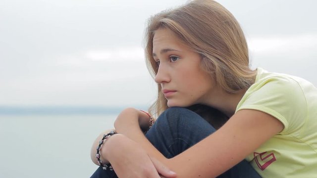 Pensive sad teen girl sitting on beach in evening