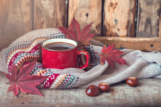 Red vintage cup of coffee with a knitted sweater, fall maple leaves and chestnuts on a wooden background