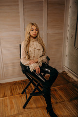 Beautiful luxurious blonde woman sitting on chair on a dark textural background. Studio shot. Girl looking in camera