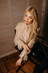 Beautiful luxurious blonde woman sitting on chair on a dark textural background. Studio shot.