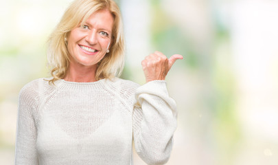 Middle age blonde woman wearing winter sweater isolated background smiling with happy face looking and pointing to the side with thumb up.