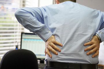 Fototapeta premium Close-up view of a office worker man with pain in kidneys. Young male with back ache clasping her hand to her lower back. Men suffering from ribbing pain, waist pain.