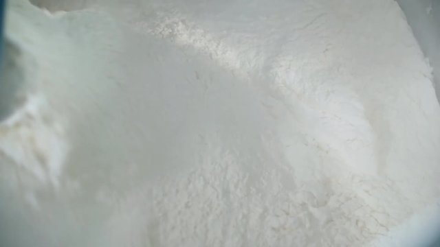 Unrecognizable factory worker adding baking flour into industrial dough kneading machine with sugar, whipped eggs and butter in it