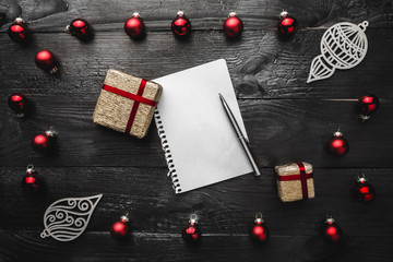 Upper, top, view from above of red evergreen toys, presents, handmade winter figurines, notepad and pen on black background, with space for text writing, greeting.