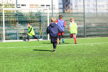  boys in red and blue, green uniforms play football with team on the green grass. Team game,...