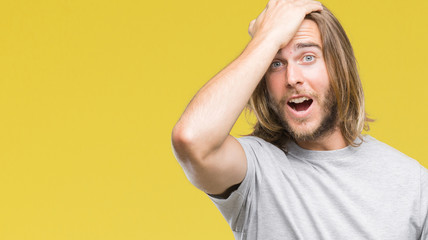 Young handsome man with long hair over isolated background surprised with hand on head for mistake,...