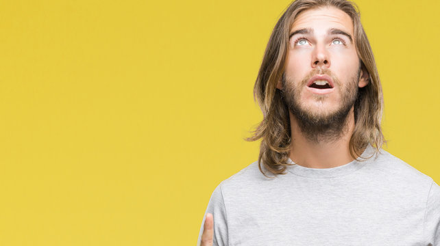 Young handsome man with long hair over isolated background amazed and surprised looking up and pointing with fingers and raised arms.