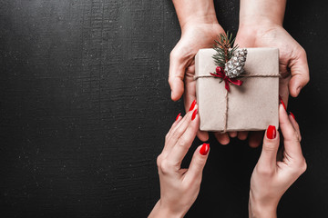On a black background, a man's hands carry a gift in the hands of a young lady. Space for a greeting message. Top view.