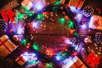 Wooden background with colored lights and stars. surrounded by gifts and cones. In the center there is space for the holiday message. Top view.