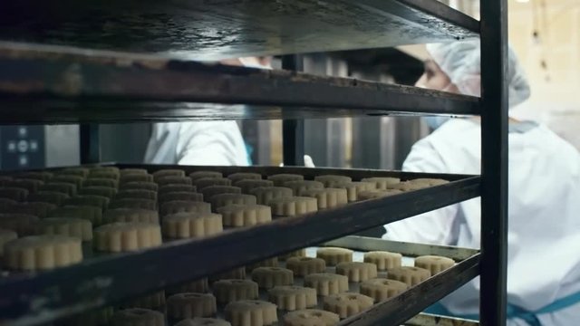 Close up shot of baking rack with trays of delicious cookies being pulled by two confectionery workers
