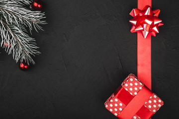 Upper top view of a red ribbon, present and evergreen branch on a stone black background, with...