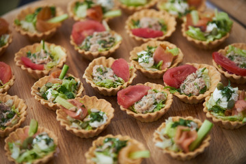 Tartlets with vegetables, chicken breast, cream and a slice of tomato on a wooden table.