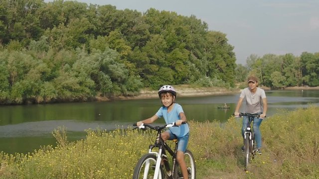 Family on bikes. A child with mother cycling in nature. A woman with a child on bicycles ride along the river.