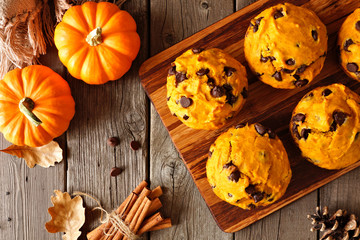 Autumn pumpkin chocolate chip muffins. Top view table scene on a rustic wood background.