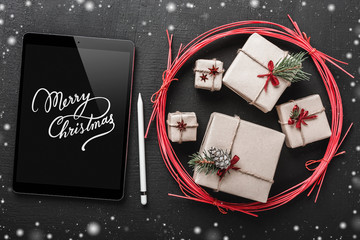 Christmas background, handmade gifts in a red circle, Merry Christmas tablet, snowflake effect. Top view.