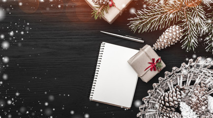 On a black background, a fir tree with cone and decorative objects. Gift and a note book or a...
