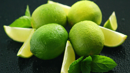 Closeup fresh bright green limes placed on dark background with water drops 