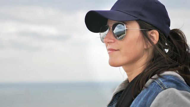Portrait of hiker casual woman in sunglasses and cap enjoying seascape at overcast weather