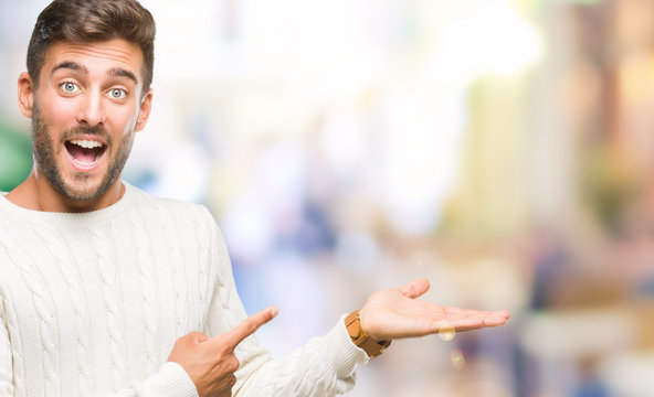 Young handsome man wearing winter sweater over isolated background amazed and smiling to the camera while presenting with hand and pointing with finger.
