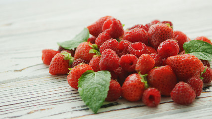 Small green leaves decorating pile of yummy ripe strawberries and raspberries lying on white lumber table
